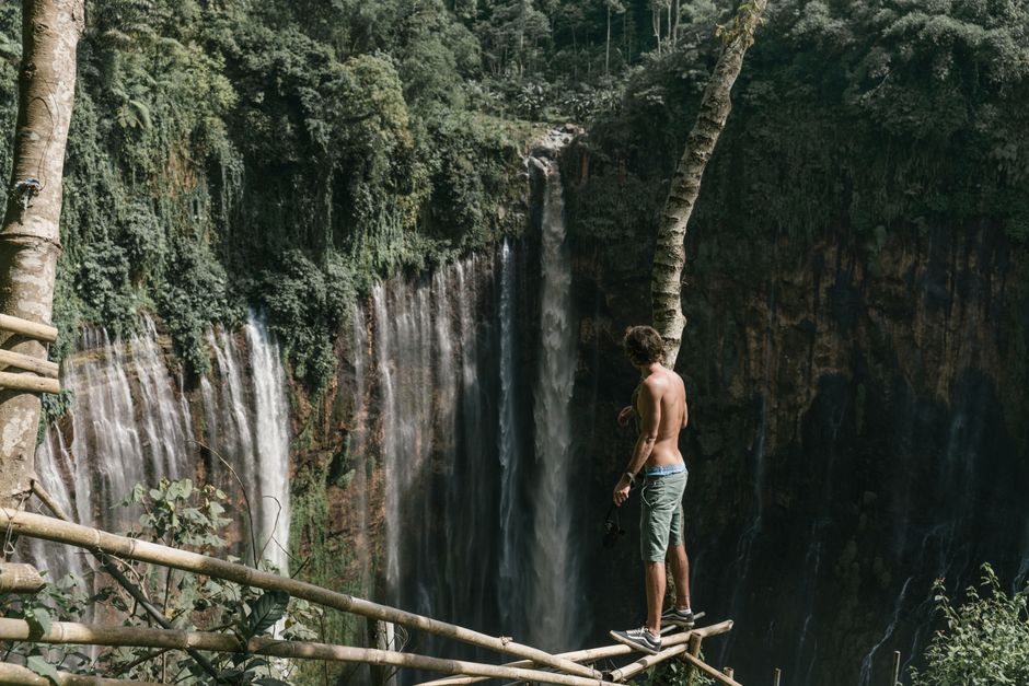 Man enjoying the breathtaking view of a majestic waterfall from a forested cliff.