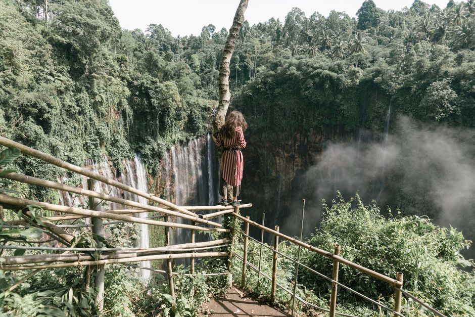 Woman standing by a waterfall in a lush forest, enjoying the breathtaking natural scenery.