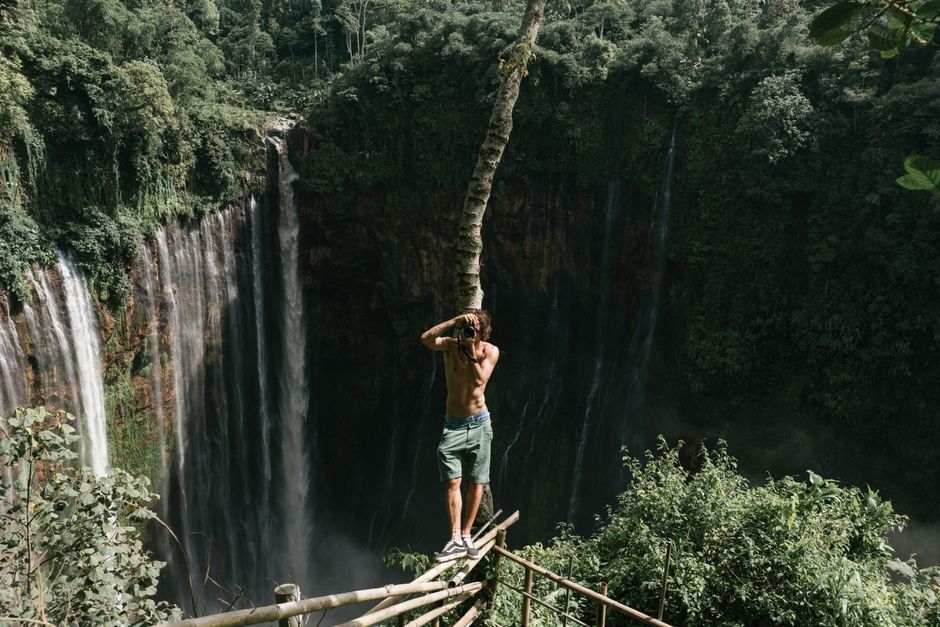 A daring photographer captures a stunning waterfall scene amidst lush greenery, showcasing adventure and nature.